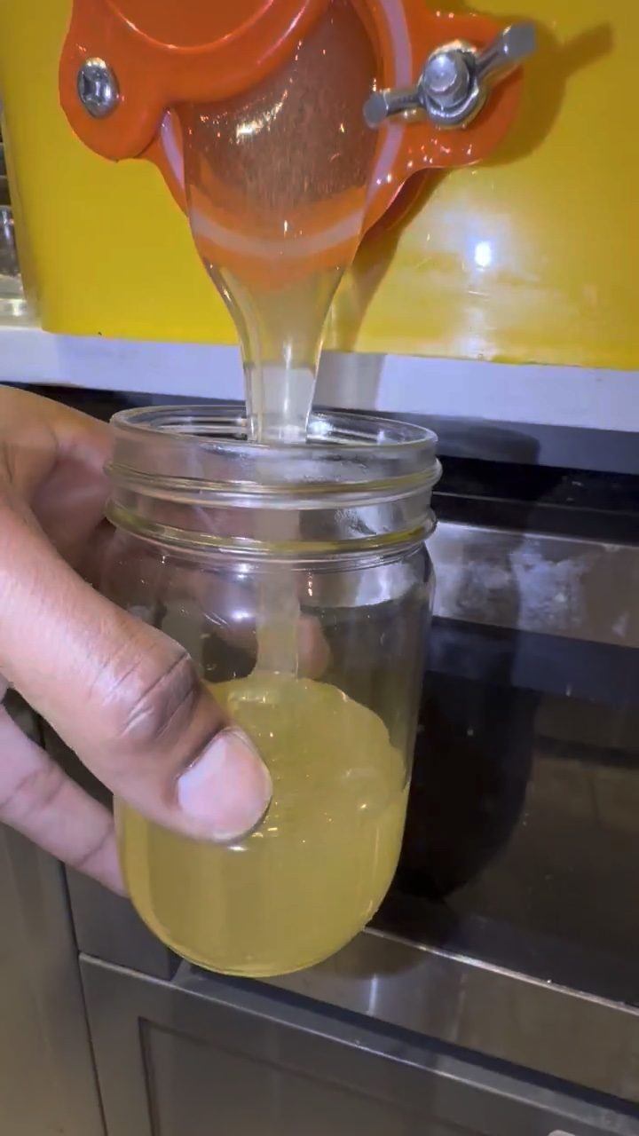Raw honey running from the tap into a jar held by hand