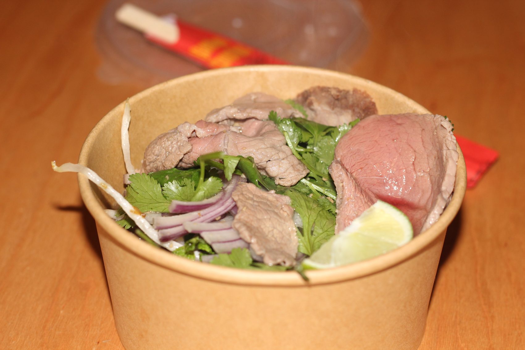 Close-up of a pho bowl — rare beef, cilantro, red onion, and lime
