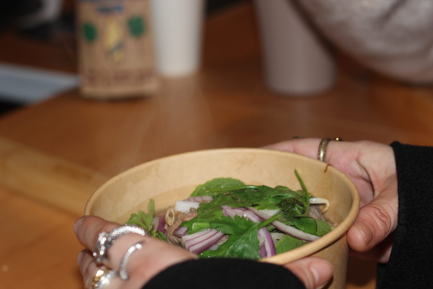Hands passing a fresh bowl of pho across the counter